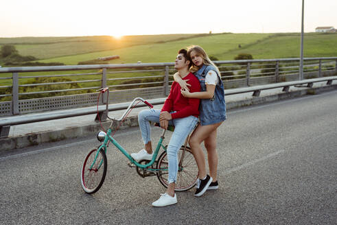 Young couple standing on bridge with vintage bicycle - ADSF03254