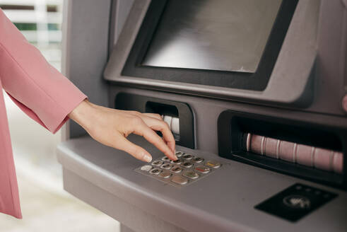 Ausschnittaufnahme einer Frau in Rosa bei der Eingabe des PIN-Codes für einen Geldautomaten, der mit einer Kreditkarte arbeitet. - ADSF03262