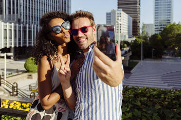 Beautiful black woman and handsome Caucasian man posing for selfie while standing on background of modern city - ADSF03322