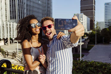 Beautiful black woman and handsome Caucasian man posing for selfie while standing on background of modern city - ADSF03323