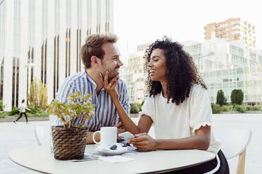Beautiful African-American woman and handsome Caucasian man smiling and looking at each other while spending time in outdoor cafe together - ADSF03328