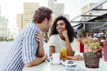 Beautiful African-American woman and handsome Caucasian man smiling and looking at each other while spending time in outdoor cafe together - ADSF03329