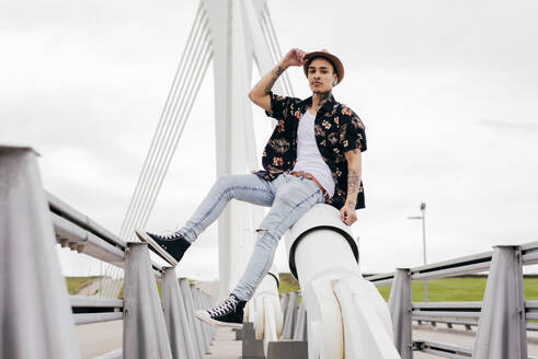 Hipster sitzt auf dem Geländer einer Brücke - ADSF03359