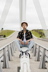 Hipster sitzt auf dem Geländer einer Brücke - ADSF03361