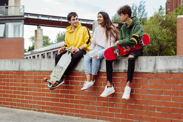 Fröhliche männliche und weibliche multiethnische Teenager sitzen mit Skateboards auf einem Zaun - ADSF03372