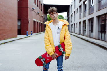 Teenager with skateboard standing on street - ADSF03380