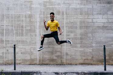 Aufgeregt verrückte ethnische Teenager Junge springen und Spaß an Betonwand auf der Straße - ADSF03387