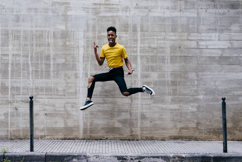 Excited crazy ethnic teenage boy jumping and having fun at concrete wall on street - ADSF03387