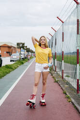 Casual teen girl in shorts and roller skates standing on lane of sports ground looking at camera. - ADSF03388