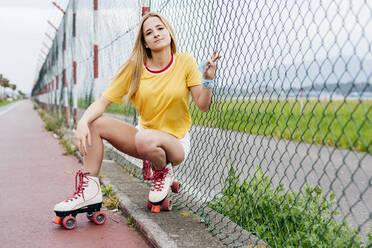 Young serious teen girl in summer stylish outfit looking at camera sitting near street net. - ADSF03389