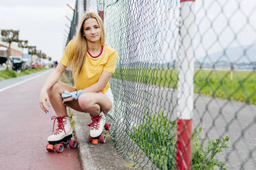 Young serious teen girl in summer stylish outfit looking at camera sitting near street net. - ADSF03390