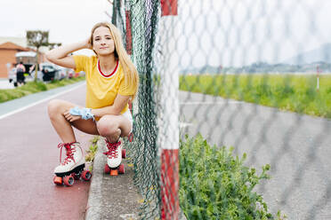 Young serious teen girl in summer stylish outfit looking at camera sitting near street net. - ADSF03391