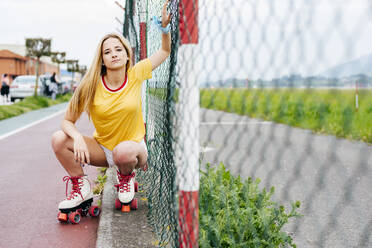 Young serious teen girl in summer stylish outfit looking at camera sitting near street net. - ADSF03392