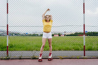 Casual teen girl in shorts and roller skates standing on lane of sports ground looking at camera. - ADSF03393