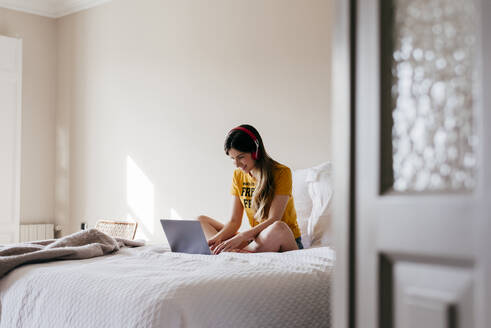 Fröhliche Frau mit Kopfhörern und Laptop - ADSF03407