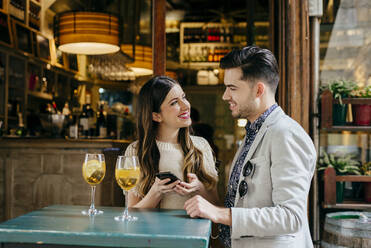 Pretty woman with smartphone interacting with stylish boyfriend while sitting in outside cafe on street. - ADSF03509