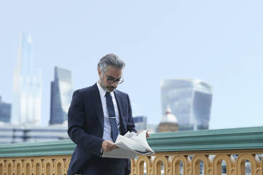 Businessman reading paper against clear sky in city - PMF01219