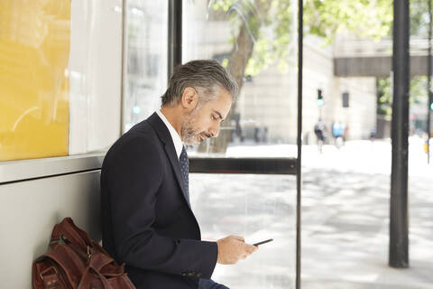 Businessman using phone while sitting at bus stop stock photo