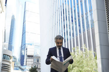 Entrepreneur reading newspaper outside office in city - PMF01234