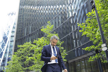 Businessman texting through mobile phone outside office building in city - PMF01247
