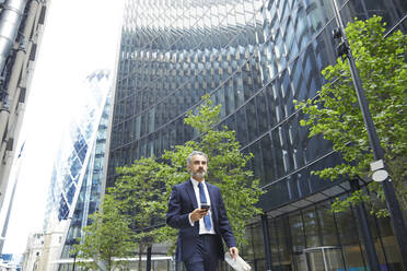 Businessman texting through mobile phone outside office building in city - PMF01248