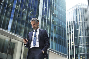 Businessman using mobile phone outside office building in city - PMF01253