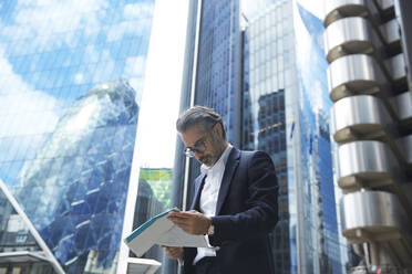 Entrepreneur reading newspaper against office building in city - PMF01257