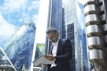 Unternehmerin liest Zeitung vor Bürogebäude in der Stadt - PMF01257