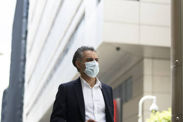 Businessman wearing protective mask in city - PMF01284