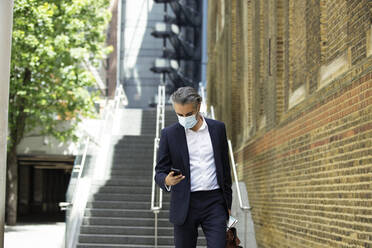 Businessman wearing mask using phone in city - PMF01285