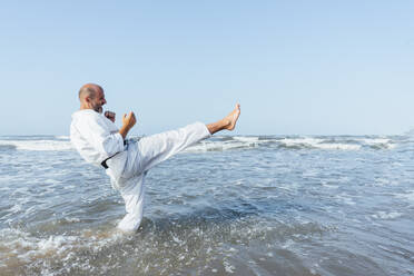 Älterer Mann, der Karate im Meer gegen den klaren Himmel übt - CJMF00321