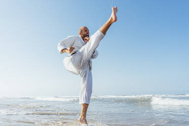 Mann schreit beim Üben von Karate im Meer gegen den klaren Himmel - CJMF00323