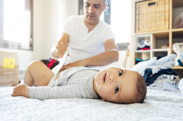 Vater mit Baby auf dem Bett liegend, Windeln wechselnd - JCMF01021