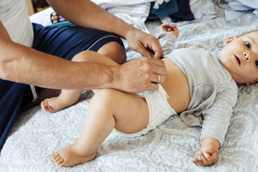 Vater mit Baby auf dem Bett liegend, Windeln wechselnd - JCMF01022