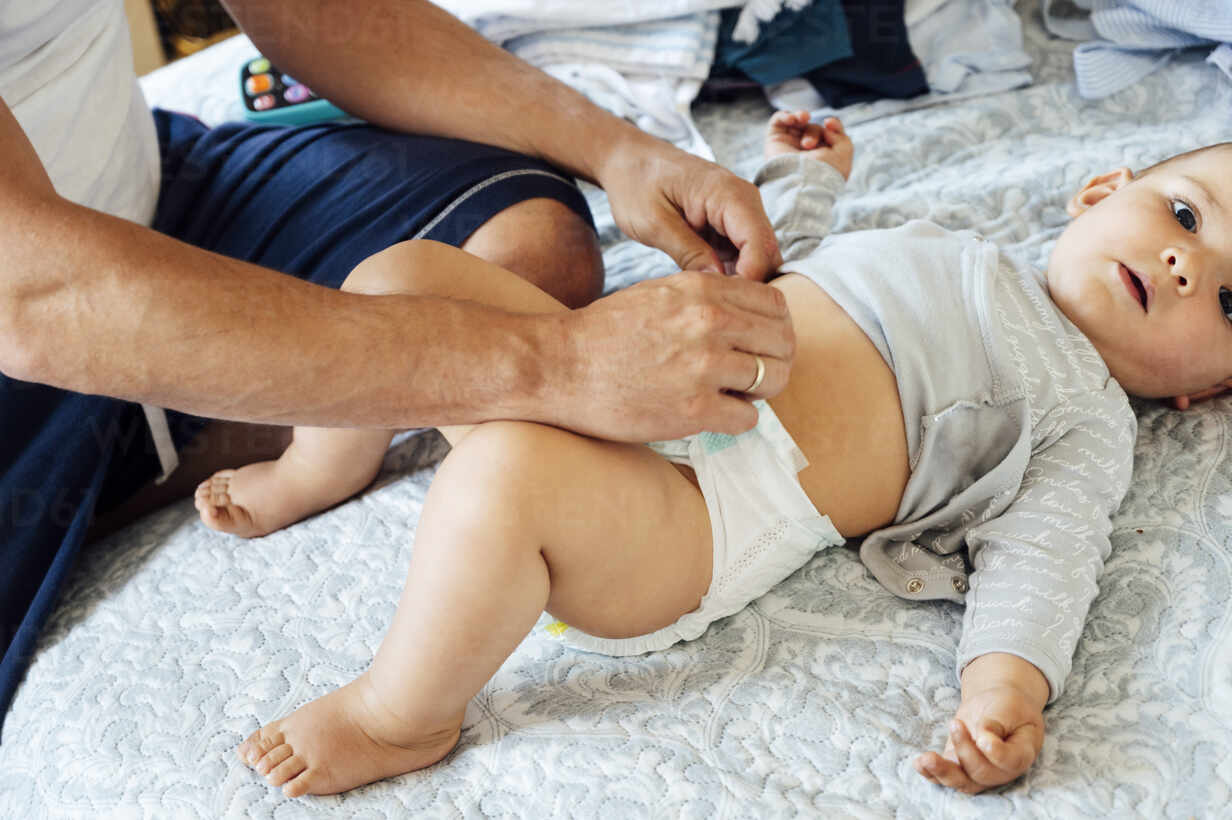 Father with baby boy lying on bed, changing diapers stock photo