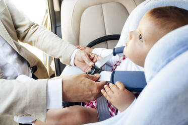Father fastening baby boy sitting in child's seat in a car - JCMF01032