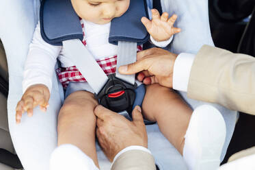 Father fastening baby boy sitting in child's seat in a car - JCMF01033