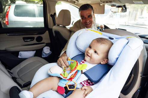 Vater befestigt Baby im Kindersitz im Auto - JCMF01035