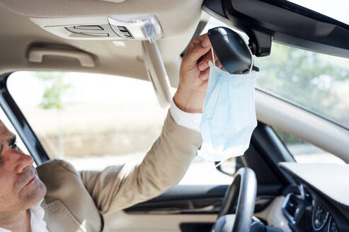 Portrait of man in car taking off his protective mask - JCMF01036