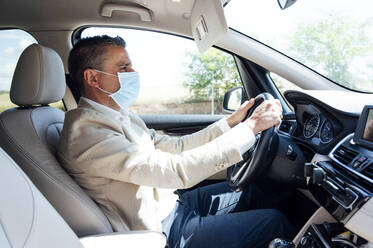 Portrait of man in car wearing protective mask - JCMF01038