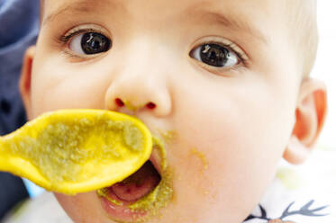 Portrait of baby boy eating, father holding spoon - JCMF01048