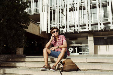 Junger Tourist, der mit seinem Smartphone spricht und auf einer Treppe in der Stadt sitzt - ADSF03588