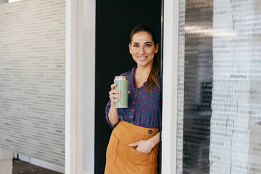 Cheerful adult woman standing in the office and looking at camera while holding cup. - ADSF03650