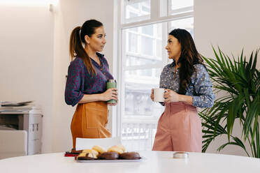 Pretty young women standing together and talking on coffee break in the office. - ADSF03651