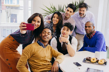 Multiracial team standing and sitting while taking selfie at the table in office. - ADSF03660