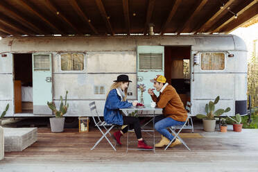 Junger Mann und Frau genießen leckeren Kuchen, während sie an einem Tisch in der Nähe eines schmuddeligen Lieferwagens sitzen - ADSF03725