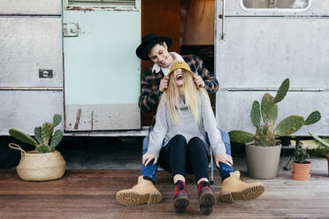 Attractive young man and woman smiling while sitting near shabby camper together - ADSF03747