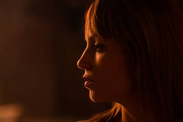 Close-up of emotionless young woman with bangs standing in soft gold light of sunset looking away - ADSF03880