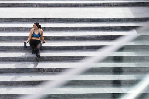 Junge sportliche Frau sitzt in der Pause auf einer Treppe - JMPF00222