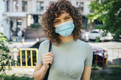 Brunette curly woman wearing protective mask in city - OYF00144